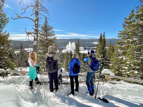 Four acrive 60 year old seniors snowshoeing in Yellowstone on a sunny winter day with Old Faithful erupting in the background.