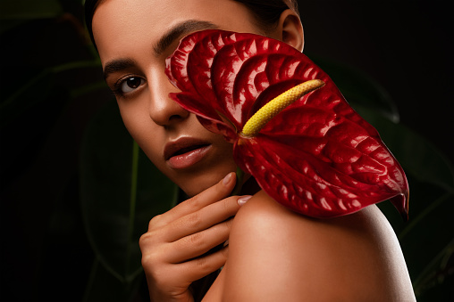 Portrait of attractive girl with healthy clean skin and beautiful make-up. Aesthetic cosmetology and makeup concept.She is holding a red flower in her hands.