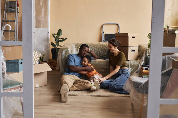 Happy young intercultural family of three relaxing on the floor by couch Happy young intercultural family of three relaxing on the floor by couch among boxes with household supplies in spacious living room real wife stories stock pictures, royalty-free photos & images