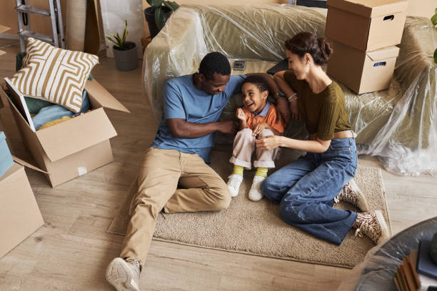 Above angle of young affectionate family sitting on the floor by couch Above angle of young affectionate family sitting on the floor by couch covered with cellophane and having fun while having short rest real wife stories stock pictures, royalty-free photos & images