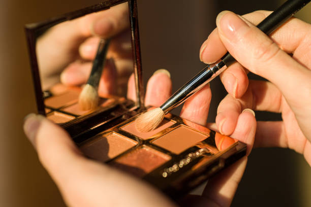 Half portrait of a young woman applying eye shadow with brush on a white studio background