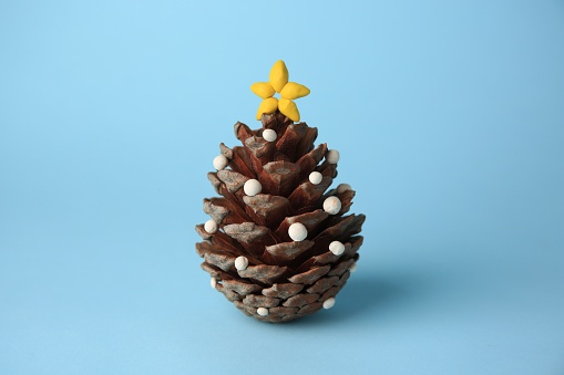 Christmas tree made from pine cone and plasticine on light blue background. Children's handmade ideas
