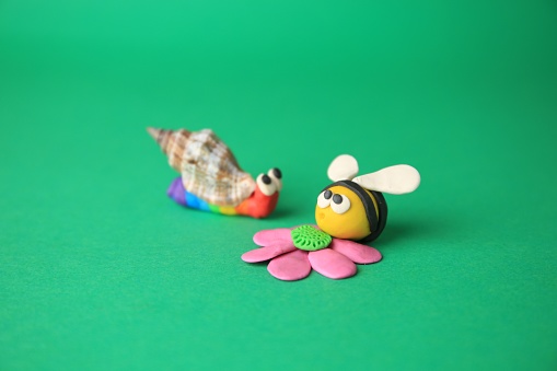 Beautiful plasticine bee with flower and snail on green background. Children's handmade ideas