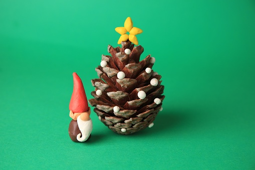 Beautiful plasticine dwarf with pinecone on green background. Children's handmade ideas