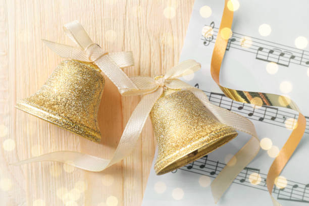 나무 탁자 위에 흰 리본과 악보가 달린 황금빛 반짝이는 종, 평평하게 놓여 있습니다. 크리스마스 장식 - bell jingle christmas music 뉴스 사진 이미지