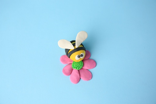 Bee with flower made from plasticine on light blue background. Children's handmade ideas