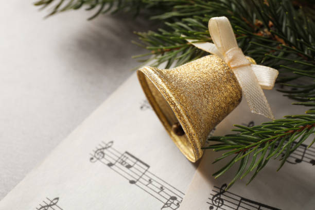 istock Golden shiny bell with bow, music sheets and fir branches on light table, space for text. Christmas decoration 1804555960