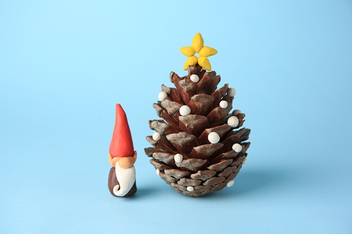 Beautiful plasticine dwarf with pinecone on light blue background. Children's handmade ideas