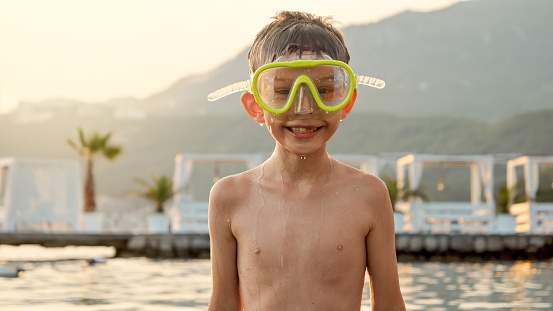 Cheerful smiling boy wearing diving mask snorkeling and swimming in the sea on sunset. Holiday, summer vacation and tourism.