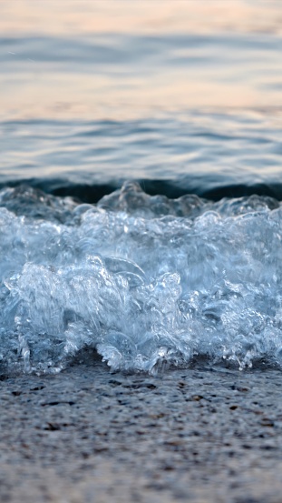 Macro tiro de olas de mar azules tranquilas rodando y rompiendo en una playa de mar al atardecer photo