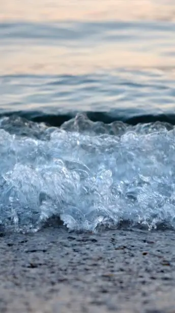 Macro shot of calm blue sea waves rolling and breaking on a sea beach on sunset.