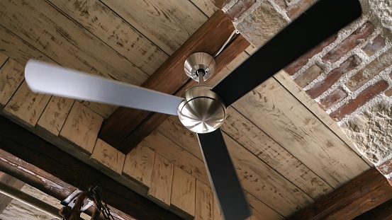 Old ceiling fan lamp spinning in the antique interior with brick walls and wooden roof.