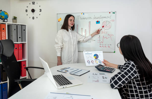 istock Two young caucasian businesswoman discussing over flipchart while explaining  business plan 1804566564