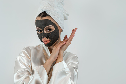 Portrait of pretty young woman wears beauty black clay mask on face isolated on white. Perfect skin concept, enjoys facial treatments