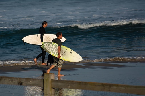 Los Angeles, United States – July 19, 2013: Two Caucasian men in casual clothing walking along a sandy beach with their surfboards