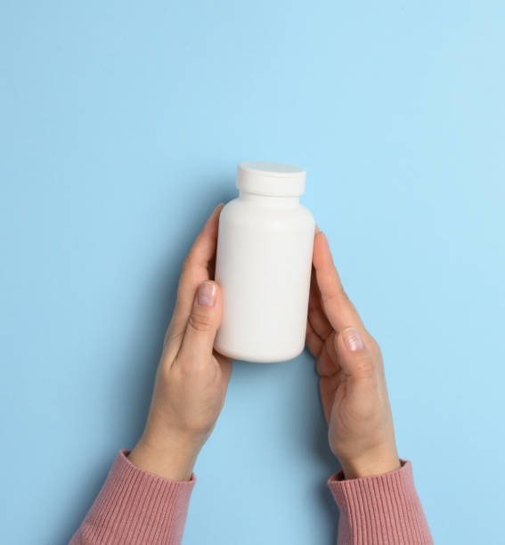 istock Two female hands holding a white plastic bottle for pills on a blue background 1804596851