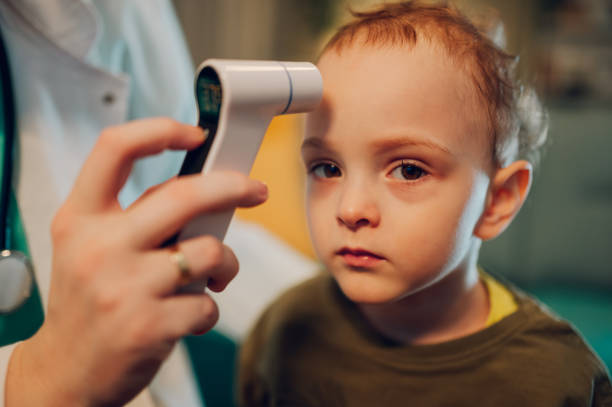istock A boy with flu sitting at home while a doctor using thermometer. 1804597447