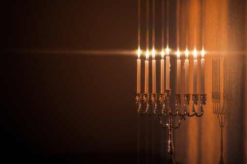 Closeup of Hanukkah menorah, or hanukkiah in the light of the sun at sunset for Jewish holiday Hanukkah. Hanukkah lamp, nine-branched candelabrum with burning candles with star filter.