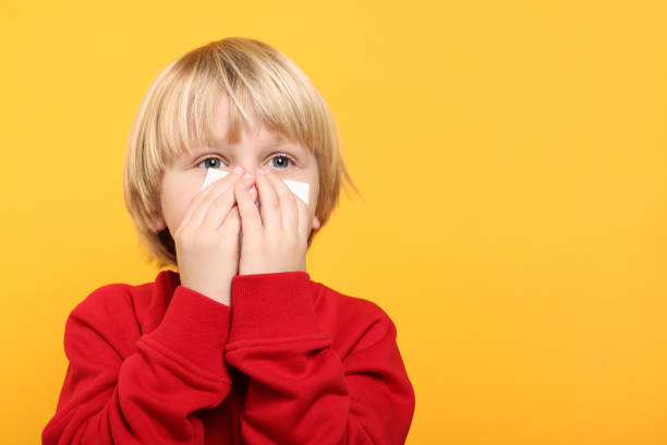 istock Boy blowing nose in tissue on orange background, space for text. Cold symptoms 1804601304