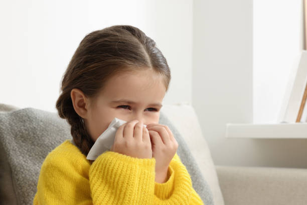 istock Girl blowing nose in tissue on sofa in room. Cold symptoms 1804604092