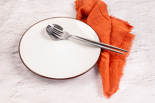 White empty plate with cutlery on orange textile napkin. Autumn table setting. Top view