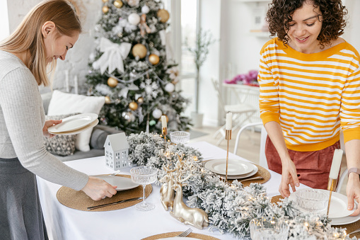 Photo of a young adult women who is hosting a Christmas party having the last preparations on the venue; setting the table and making sure everything's ready.