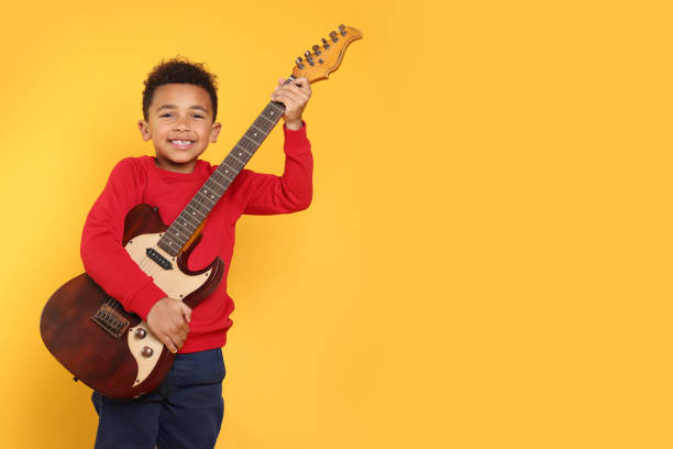 African-American boy with electric guitar on yellow background. Space for text