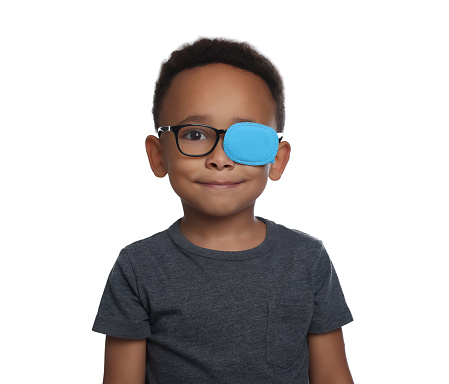 African American boy with eye patch on glasses against white background. Strabismus treatment
