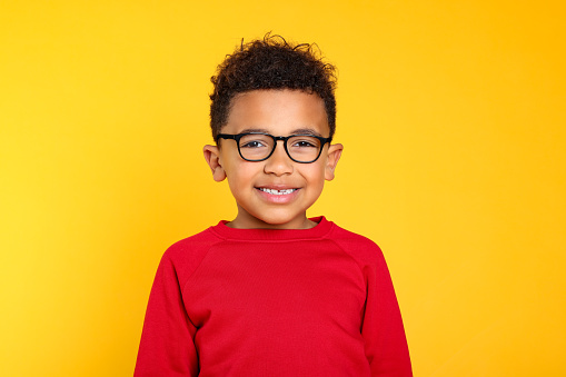 Portrait of cute African-American boy with glasses on yellow background