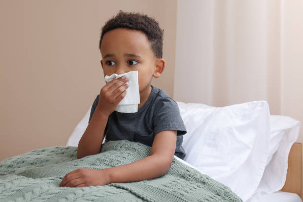 istock African-American boy with tissue blowing nose in bed indoors, space for text. Cold symptoms 1804624423