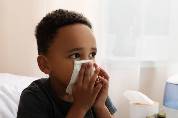 istock African-American boy with tissue blowing nose in bed indoors, space for text. Cold symptoms 1804624448
