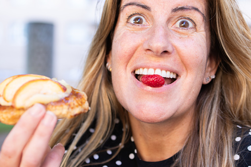 adult Caucasian woman with a sweet tooth eating the cherry of an apple pie with a playful and happy attitude.person biting a candied wild blackberry.woman making funny grimaces.