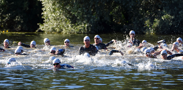 Full length side view of Hispanic sportswoman in wetsuit, swimming cap, and goggles running from water onto beach after workout in Mediterranean.