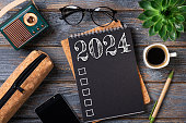 New year resolutions 2024 on desk. 2024 goals list with notebook, coffee cup, plant on wooden table. Resolutions, plan, goals, action, checklist, idea concept. New Year 2024 resolutions