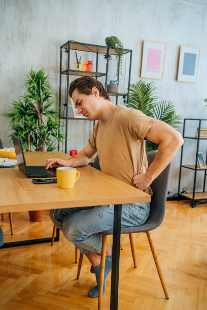 istock Young man suffering from back pain while working at home 1804663823