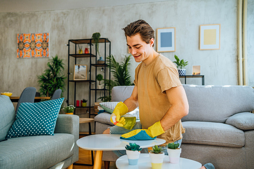 Young man cleaning coffee table in his apartment