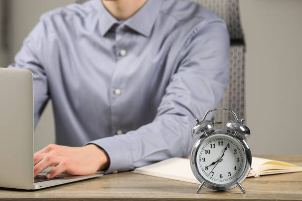 istock Silver alarm clock and man working at wooden table, closeup 1804679375
