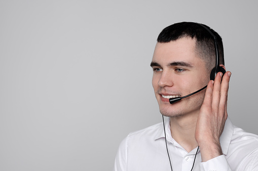 Hotline operator with headset on light grey background, space for text