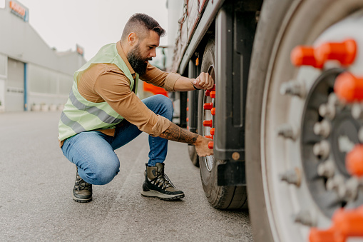 A truck driver stands beside his truck, engaged in a careful examination, affirming the vehicle's readiness for the long haul