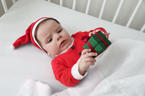 Cute baby wearing festive Christmas costume with gift box in crib