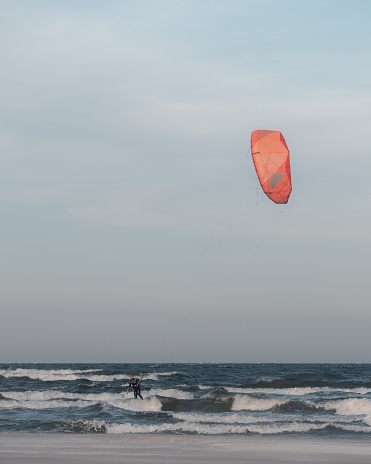 Ystad, Sweden – July 20, 2022: A kite is soaring in the sky above a beach, where a surfer has just finished riding a wave