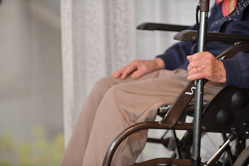 A senior woman sitting in a wheelchair with a cane and looking outside through the window
