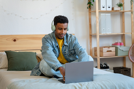 african american man in headphones using laptop on bed at home