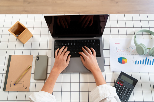 Top view of female hands typing on laptop keyboard at table in office