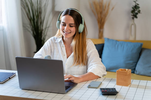 istock Smiling young woman in headphones using laptop while sitting at table at home 1804803889