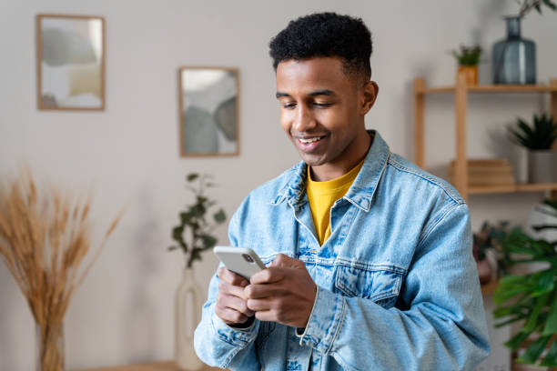 smiling african american man in denim jacket using smartphone at home