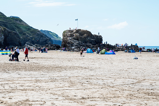 Perranporth, United Kingdom - June 1 2022: People in tents on sandy beach in Cornwall, South West, United Kingdom. View of the beach, blue sea and cliffs. Selective focus