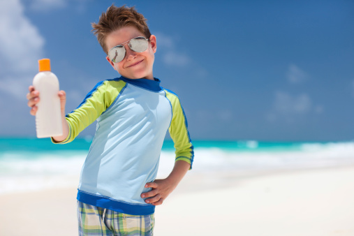Cute little boy at tropical beach holding a bottle of sunblock