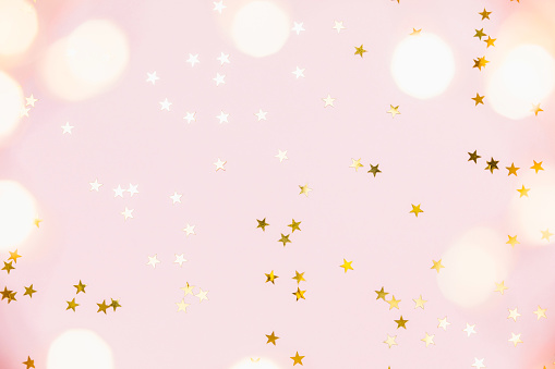 Christmas festive background. Gold party decorations, confetti stars, christmas lights on pastel pink background. Christmas, winter holiday, new year concept. Flat lay, top view, copy space