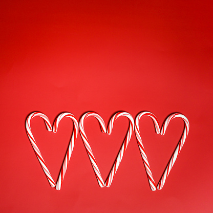 Candy cane hearts on red background. Flat lay design.